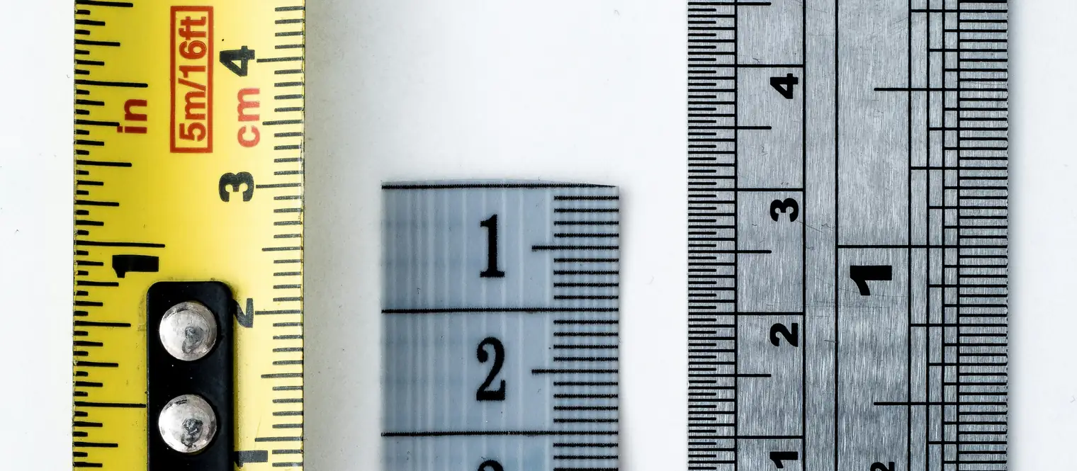 A steel tape measure and two rulers laid side by side on white, the tape marked in both inches and centimetres.
