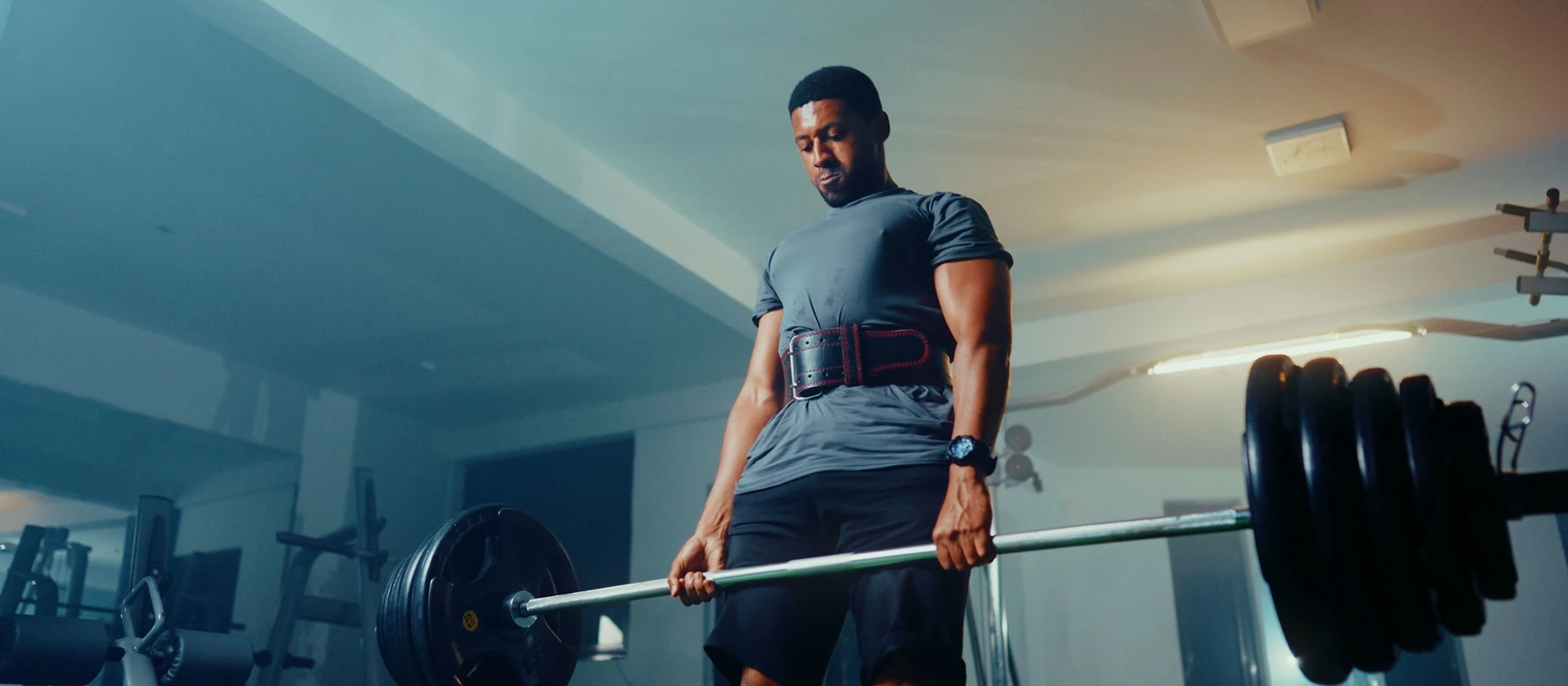 Man wearing a weightlifting belt holding a heavily loaded barbell at the top of a deadlift.