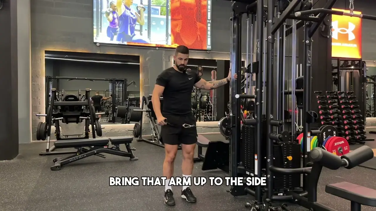 Person performing a standing single-arm cable lateral raise, holding a low pulley handle beside their hip while using the opposite hand for support, targeting the shoulder muscles.