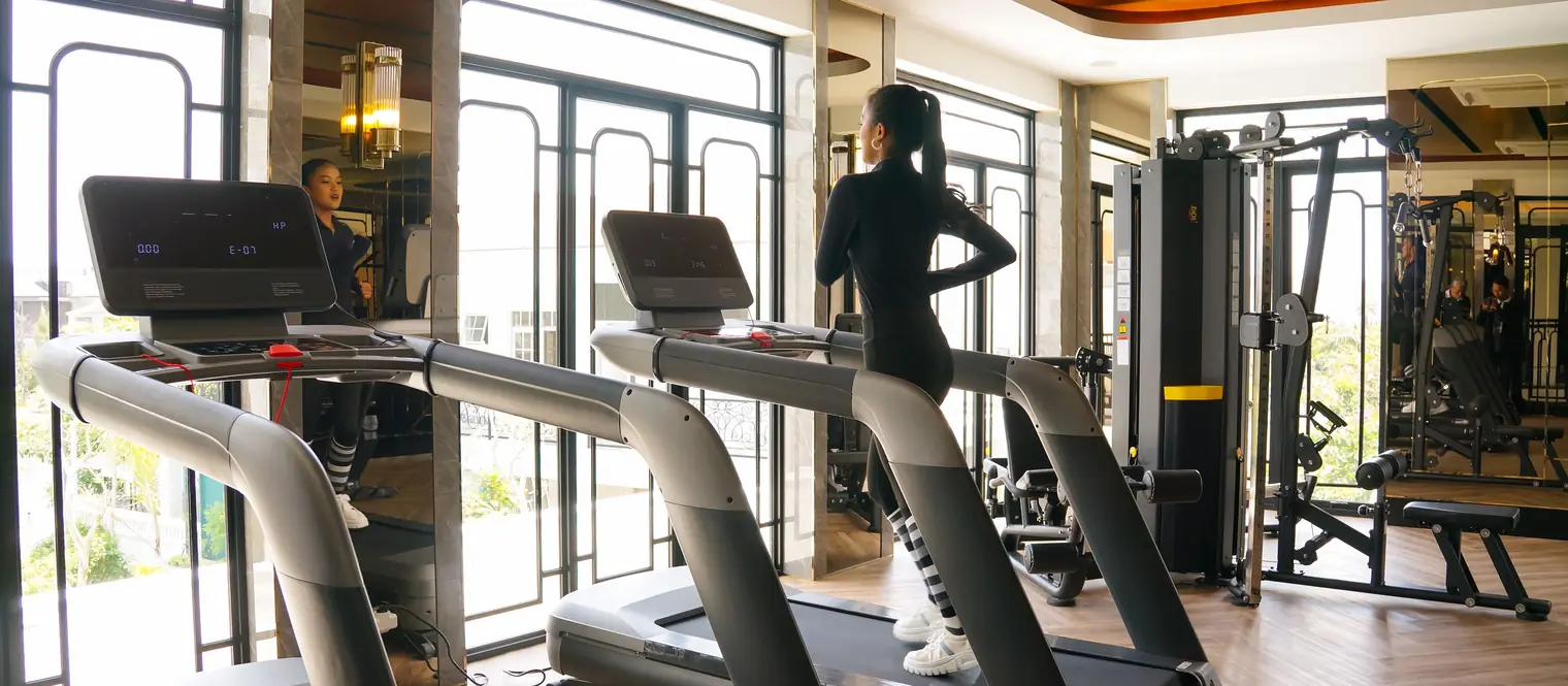 Woman walking on a treadmill in a gym, with strength training machines visible nearby.