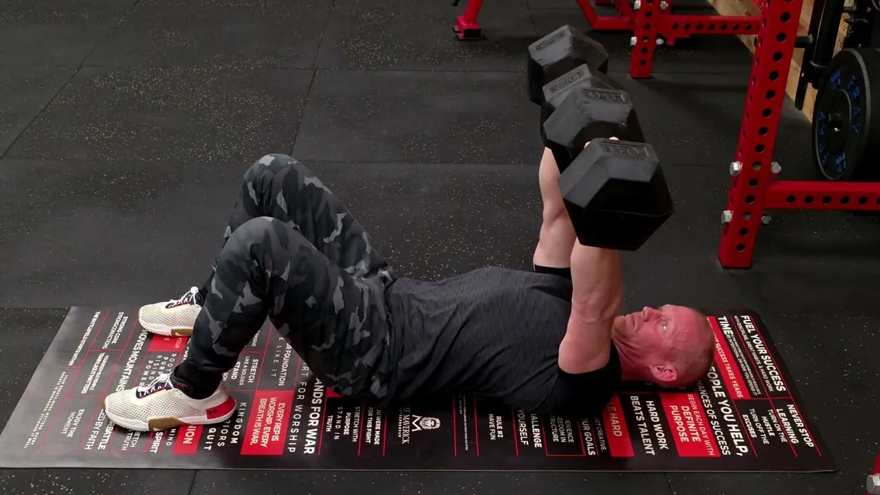 A man lying on the floor performing a dumbbell floor press. 