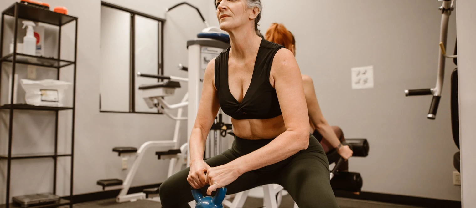 Older woman performing a kettlebell squat during a strength training workout at the gym.