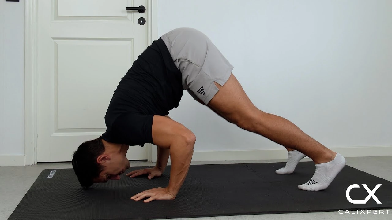 Person performing a pike push-up on an exercise mat, keeping hips raised in an inverted V position while bending the elbows and lowering their head toward the floor to strengthen the shoulders.