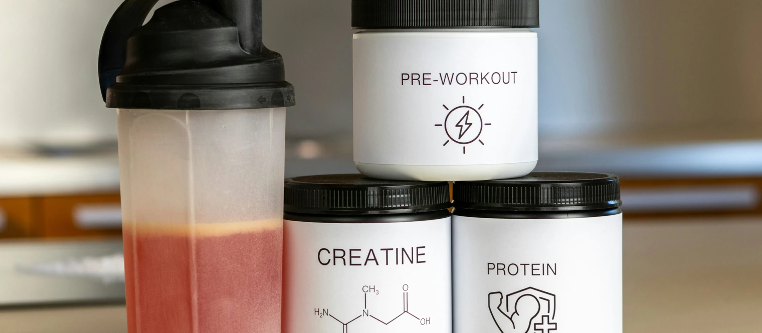 Pre workout, creatine and protein powder stacked up next to a shaker with pre-workout
