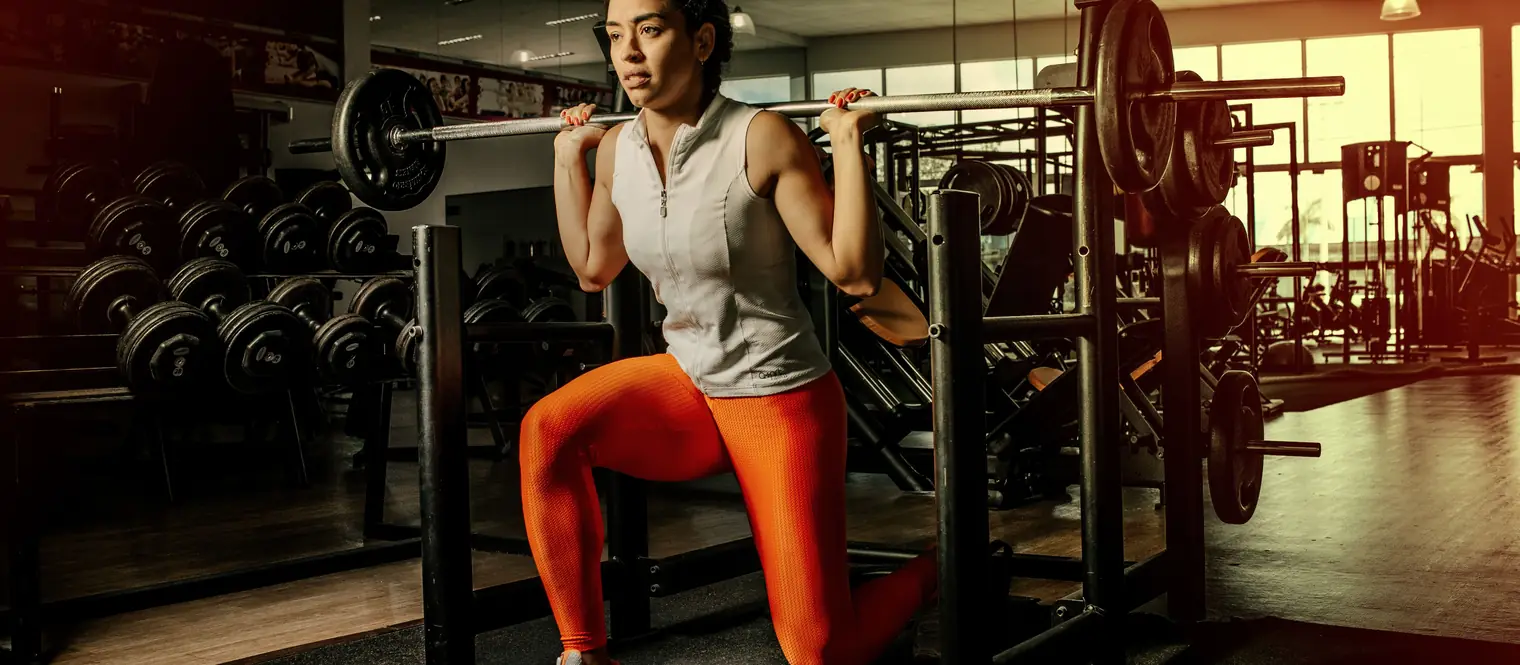 Woman performing a barbell lunge in a gym, with her rear knee lowered toward the floor.