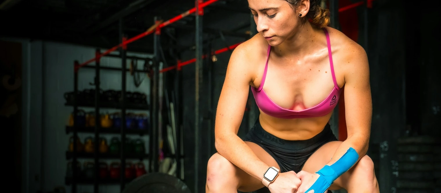 A woman sitting in the gym with tape on her arm and hand.