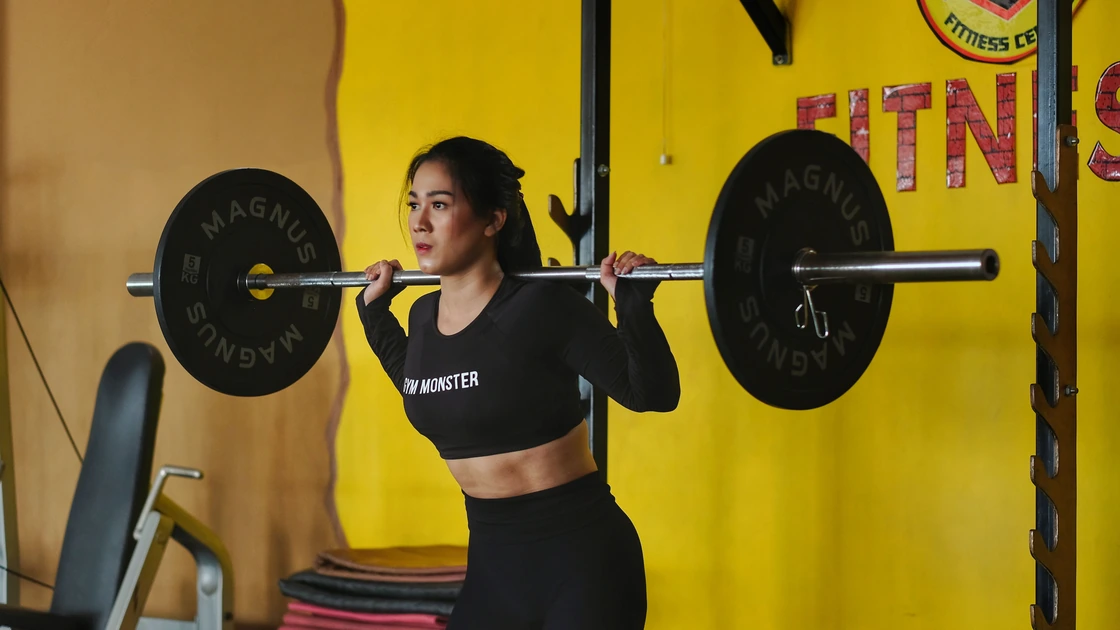 Woman preparing for a barbell back squat with weights across her shoulders in a gym.