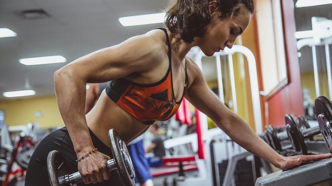 Woman performing a dumbbell row during a strength training workout at the gym.